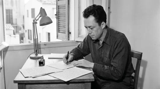 Albert Camus écrivant à son bureau près d'une fenêtre méditerranéenne, photographie documentaire noir et blanc années 1940
